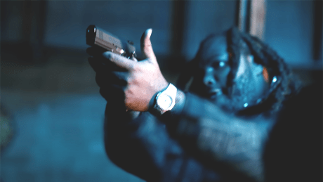 Mann (Tee Grizzley) mit halslangen Dreadlocks zielt mit einer Handfeuerwaffe