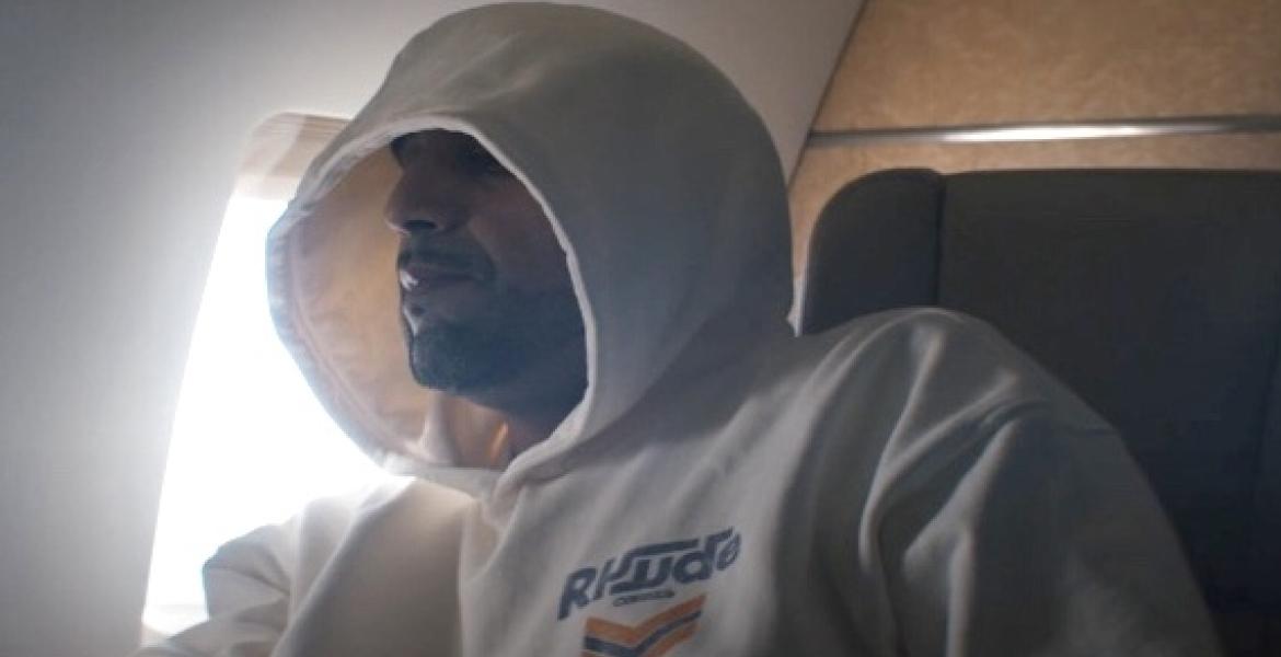 Ali As sitzt in einem weißen Hoodie in einem Flugzeug
